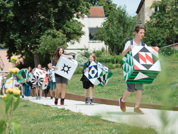 Kinder tragen große bunte Würfel und laufen einen Weg entlang.