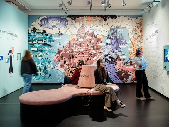Menschen stehen und sitzen vor einer großen grafischen Comic-Wand mit Burganlage
