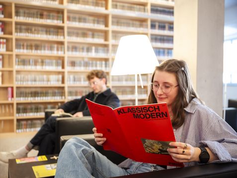 Zwei Personen lesen entspannt in Sesseln in einer gemütlichen, hellen Sitzecke in der Bibliothek.