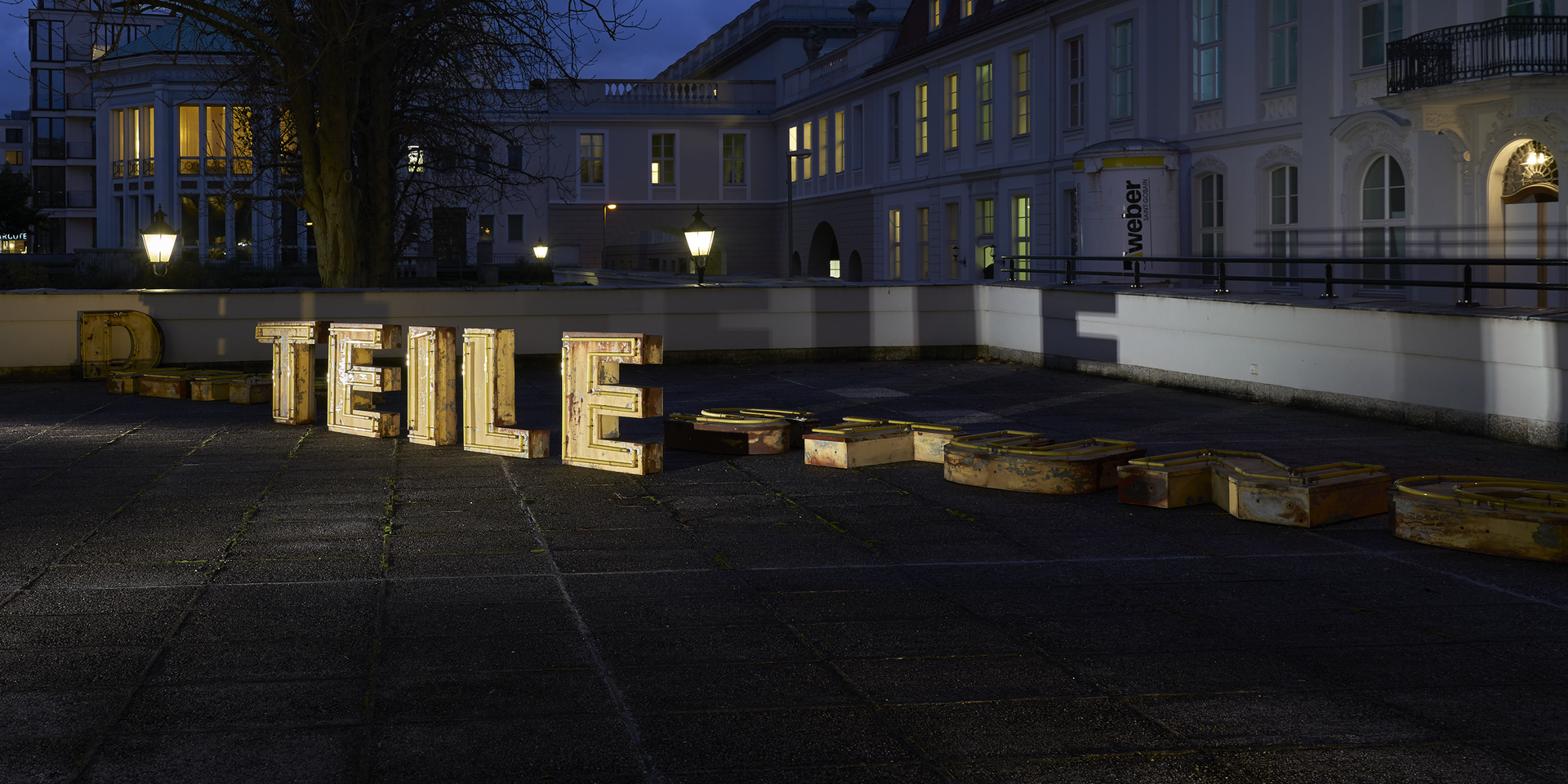 beleuchtete Installation bestehend aus Buchstaben, die "Teile" ergeben, befindet sich auf einer Dachterrasse