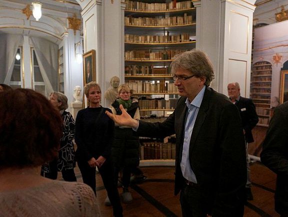 Ein Mann hält einen Arm hoch und spricht zu mehreren Menschen.