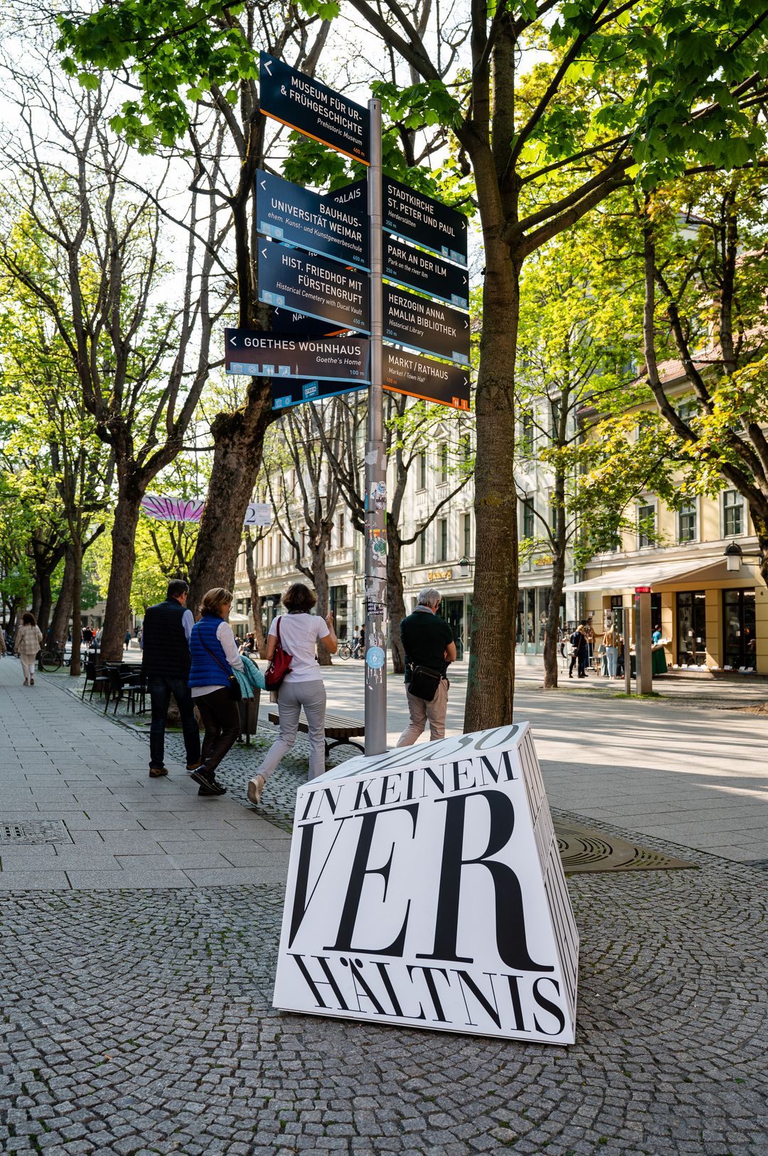 Skulptur mit Wortgebilden, die ein beim Lesen ein Zitat von Ottilie von Goethe ergeben; im Hintergrund laufen Passanten vorbei