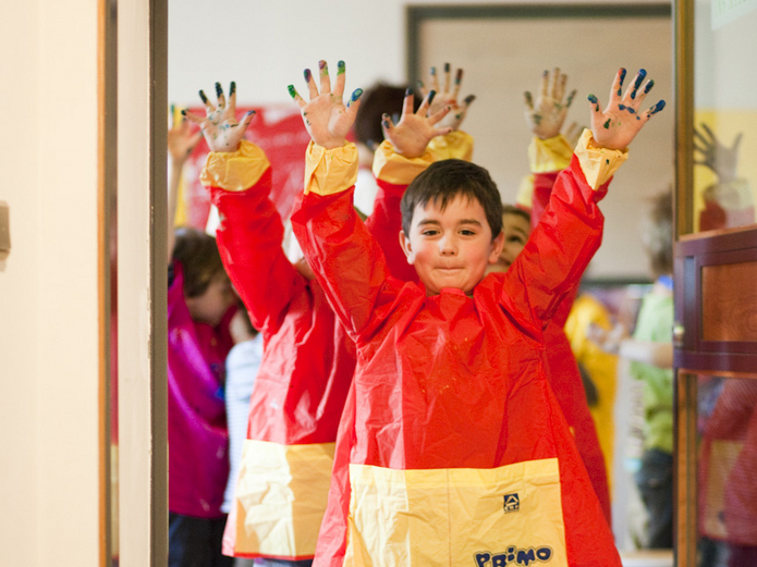 Children wearing red aprons stretch out their painted hands