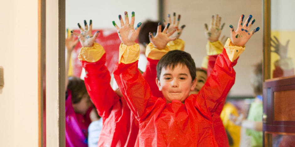 Children wearing red aprons stretch out their painted hands