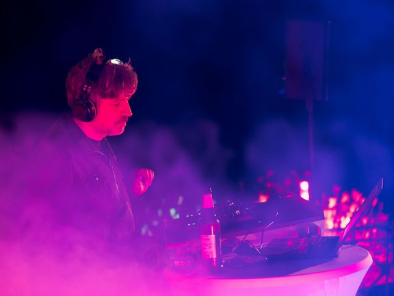 DJ Solstik spielt in rosa-blauem Nebel getaucht am Mischpult sein DJ-Set.