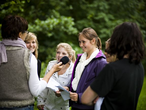 An adult interviewing young people in the park who are having a good time 