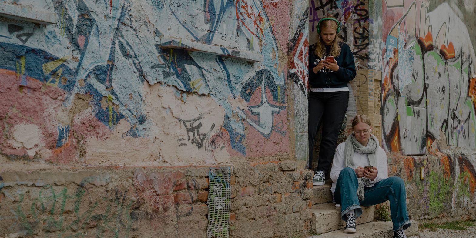 Vor einer Hauswand mit viel Graffiti steht eine Gruppe von vier Personen, die gebannt auf ein Smartphone schauen und Inhalte der Kulturapp abspielen.