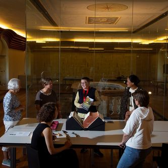 Mehrere Damen stehen um einen Tisch und schaue sich ein historisches Buch an. 