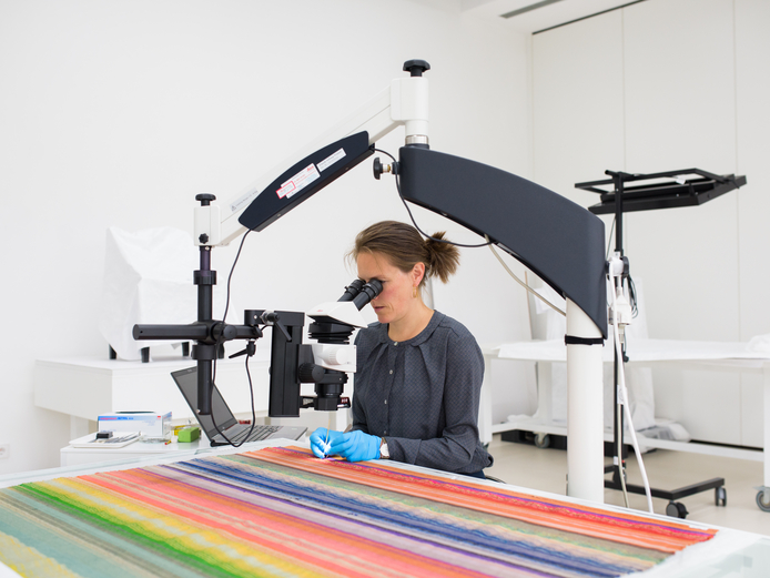 A conservator works on restoring a rug in the textile workshop