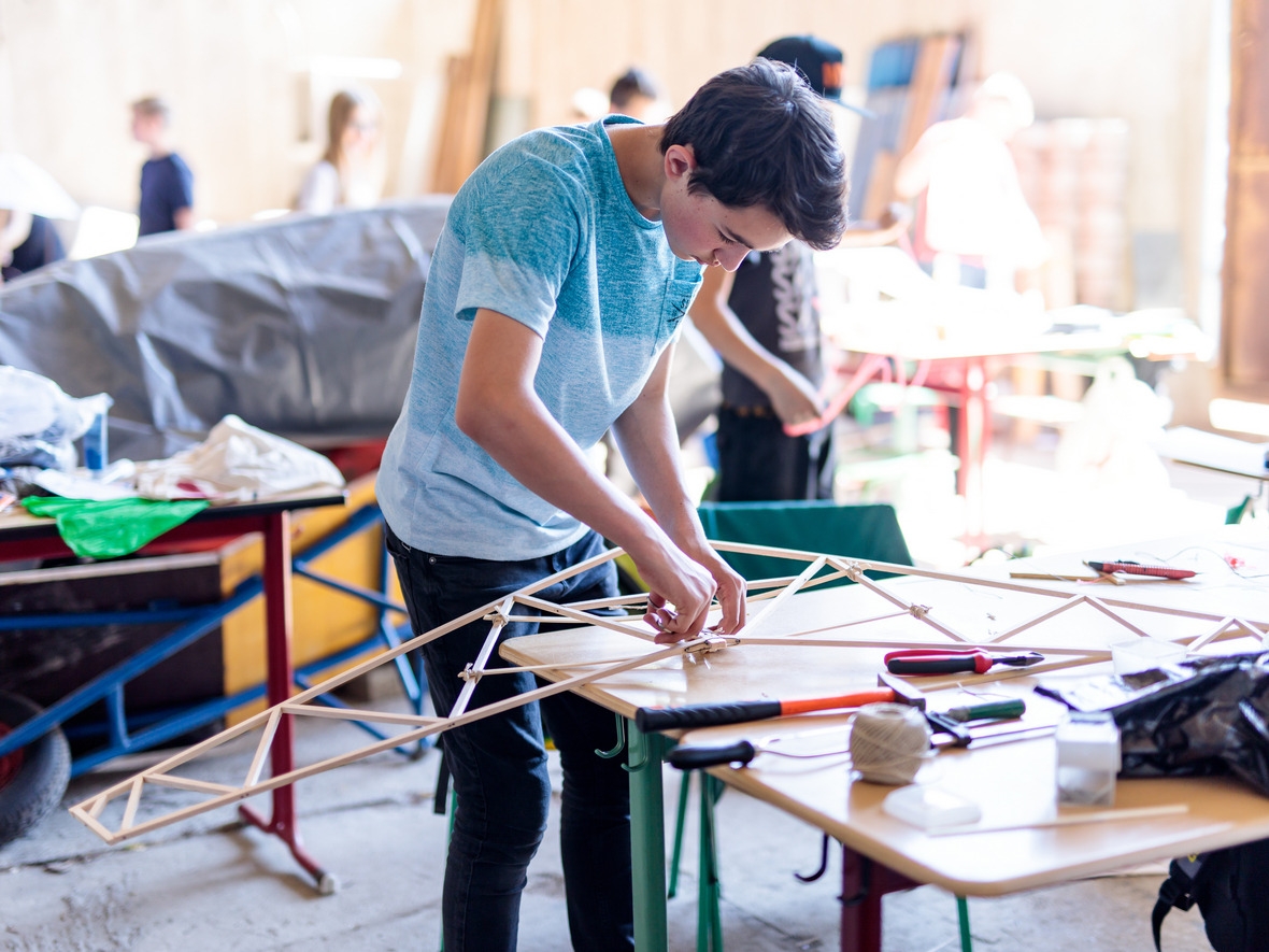 Junge bastelt an Holzkonstruktion in einer Werkstattkulisse