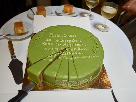 Eine grüne, angeschnittene Torte, die mit dem Goethe-Zitat "Kein Genuss ist vorübergehend, denn der Eindruck, den er hinterlässt, ist bleibend." verziert ist.