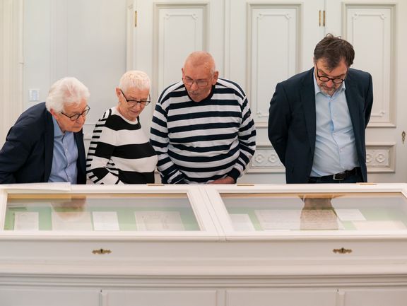 Vier Personen betrachten Manuksripte, die in zwei Glasvitrinen ausgelegt sind.