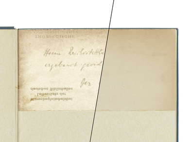 Auf einer Buchseite ist eine handschriftliche Widmung zum Teil lesbar, der andere Teil der Widmung ist überklebt.  