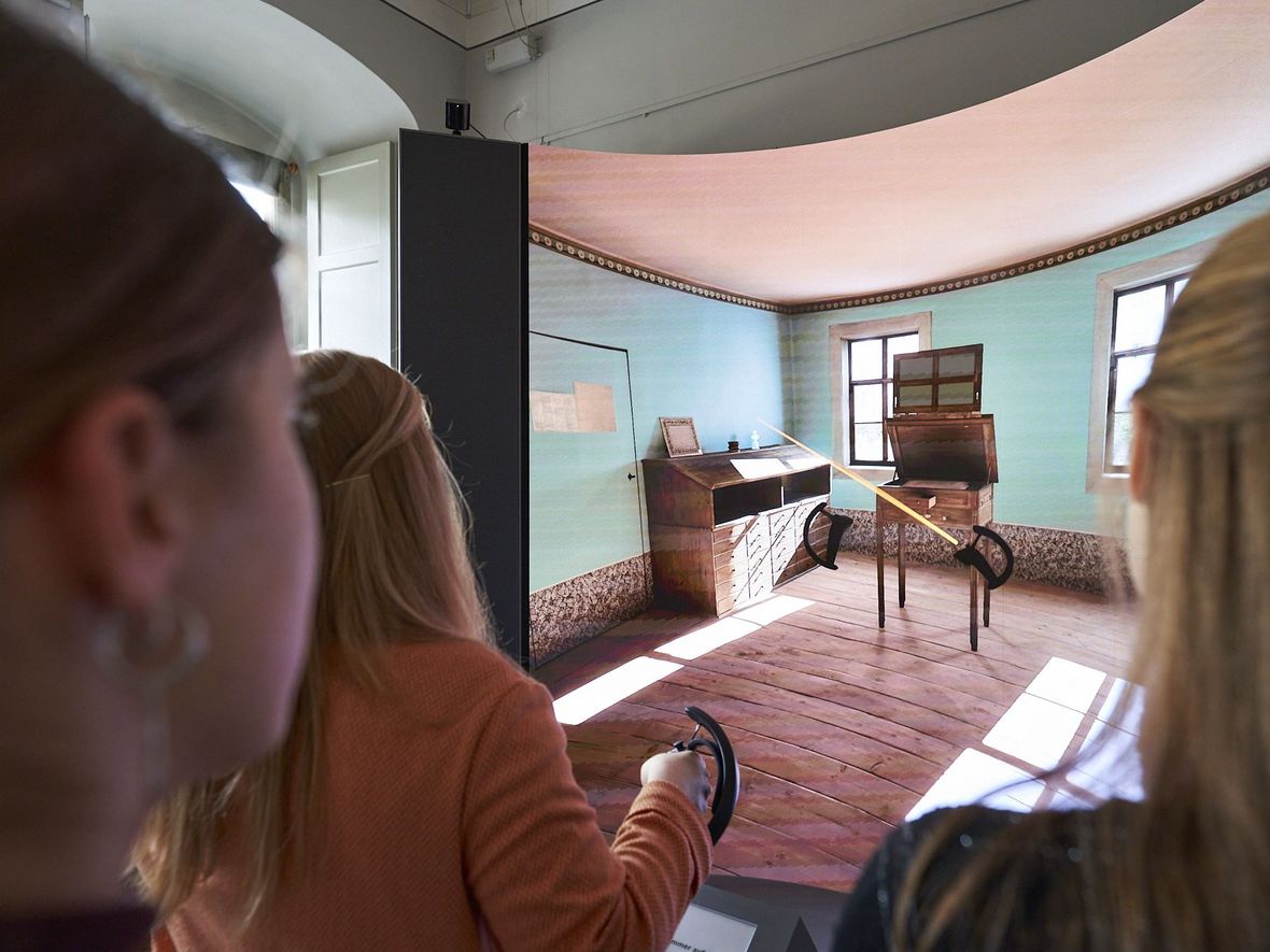 Blick über die Schulter von drei Personen auf einen großen Screen, auf dem Goethes virtuelles Arbeitszimmer zu sehen ist.