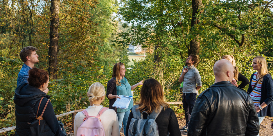 Gruppe Erwachsener steht um einen Guide in einer Parkkulisse