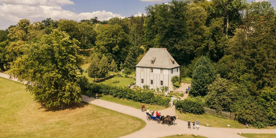 Luftaufnahme von Goethes Gartenhaus und Gehweg, auf der eine Kutsche mit Pferden fährt