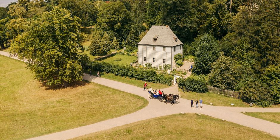 Luftaufnahme von Goethes Gartenhaus und Gehweg, auf der eine Kutsche mit Pferden fährt