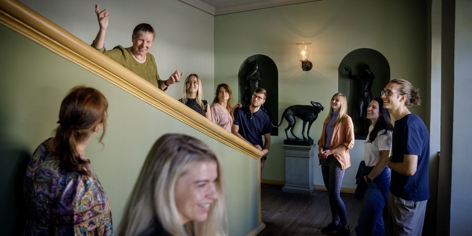 Un groupe avec un guide s'arrête sur un escalier pour observer des sculptures et des peintures.