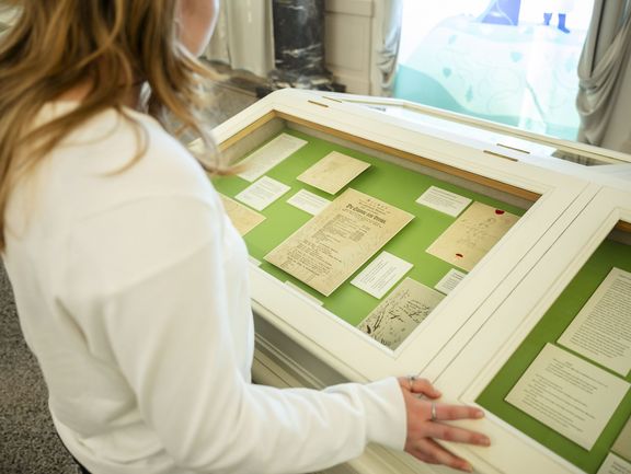 Eine Person im weißen Shirt steht vor einer Vitrine mit alten Handschriften