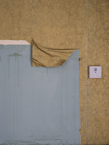 A beige wall with wallpaper falling down