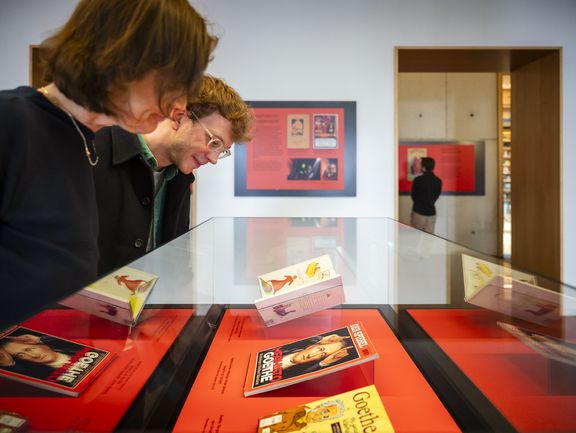 Zwei Personen sehen sich in einer Vitrine Mephisto-Illustrationen in Büchern an.