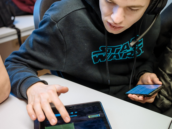 Ein Junge sitzt mit Kopfhörern am Tablet und bearbeitet eine Tonspur.