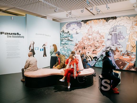 Menschen sitzen auf einer Sitzinsel und Hockern und tragen Kopfhörer.