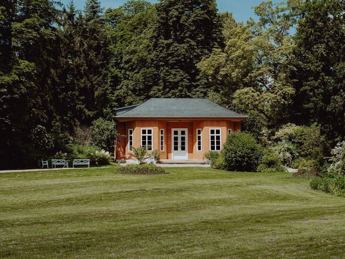 Bild von einem Pavillon umgeben von Bäumen und grüner Wiese.