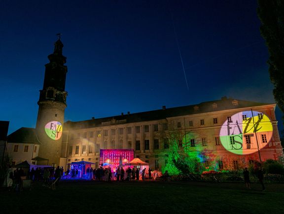 Ein Schloss wird bei Dunkelheit mit bunten Lichtkegeln beleuchtet.