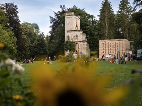 Ansicht des steinernen Tempelherrenhauses und des hölzernen Grünen Labors mit Menschen auf der Wiese