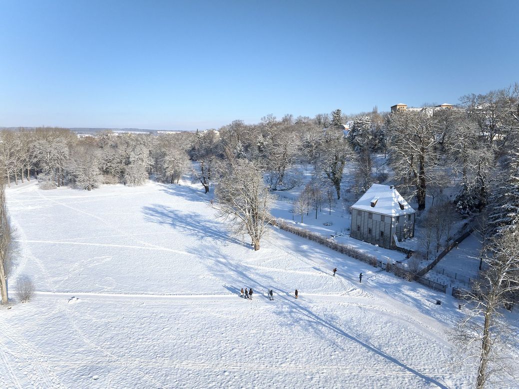 Blick von oben auf eine große eingeschneite Parklandschaft mit einem Haus im rechten Bildrand.