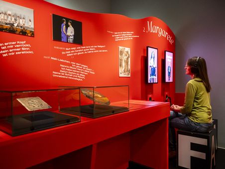 Eine große rote Wand mit Texten, Grafiken und Objekten im Glaskasten