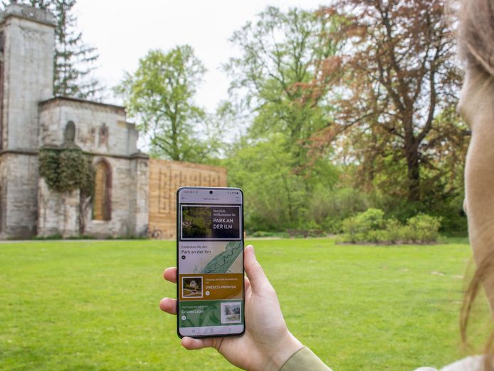 Frau hält Smartphone mit geöffneter Weimar+ App in Richtung Tempelherrenhaus