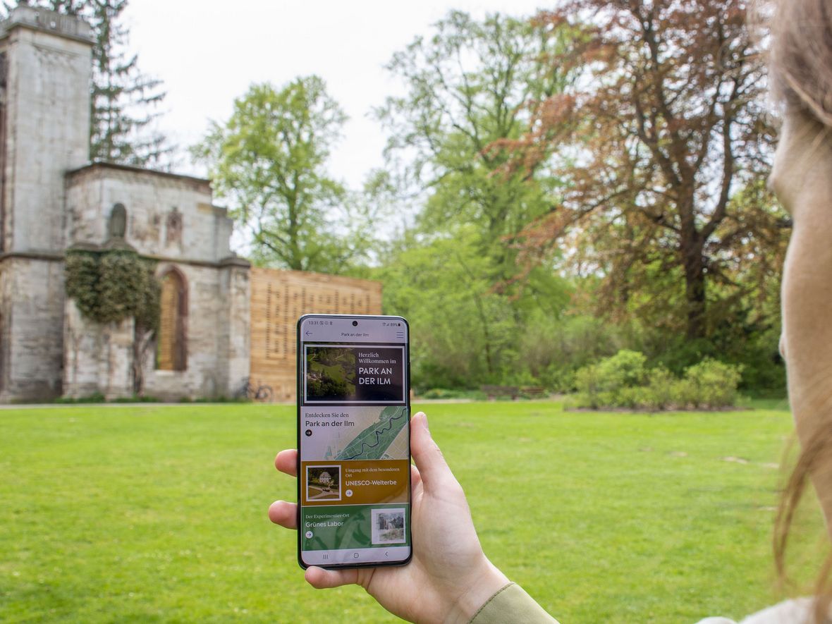 Frau hält Smartphone mit geöffneter Weimar+ App in Richtung Tempelherrenhaus