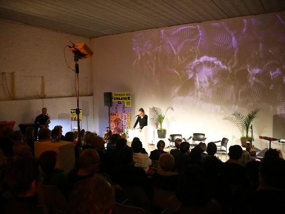 Eine Frau steht vor Publikum und spricht in ein Mikrofon.