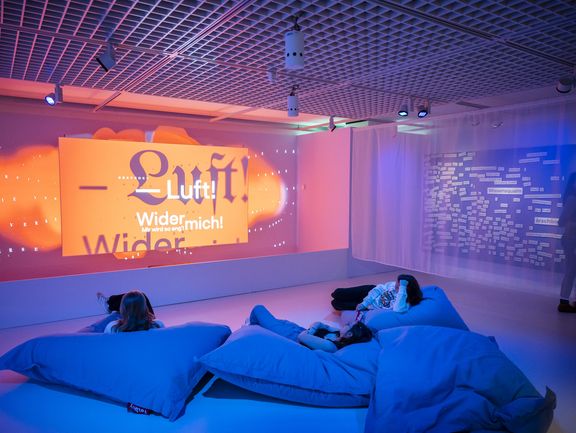 Menschen liegen auf Sitzkissen vor einer großen Leinwand