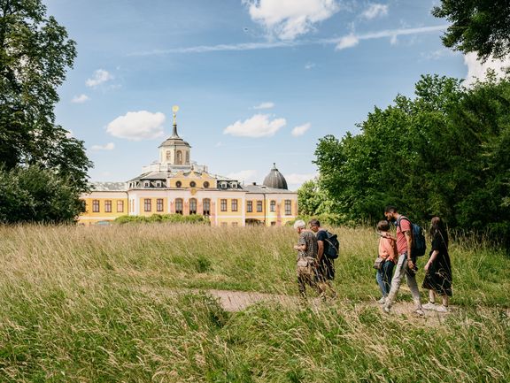 Entlang hochgewachsener Sommergräser macht sich eine Gruppe auf den Weg zum Schloss