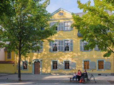 Auf einer Bank vor Schillers Wohnhaus sitzen Menschen.