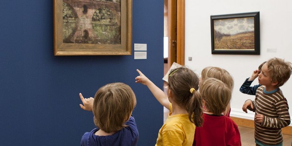 Kinder stehen gemeinsam vor einem Gemälde vor einer dunkelblauen Wand