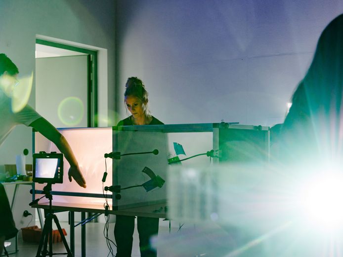 Zwei Personen machen Lichtexperimente. In der Bildmitte stehen große beleuchtete Kästen, ein Tablet filmt sie.