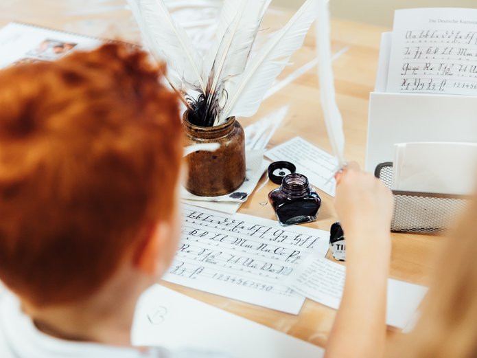 Ein Junge sitzt am Tisch und schreibt mit Federkiel und Tinte
