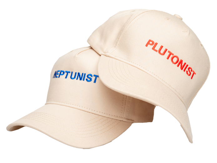 Zwei beige Baseballkappen liegen nebeneinander. Die linke Kappe hat das Wort "NEPTUNIST" in blauer Schrift auf der Vorderseite, während die rechte Kappe das Wort "PLUTONIST" in roter Schrift trägt. Beide Kappen haben einen klassischen Schirm und eine verstellbare Rückseite.
