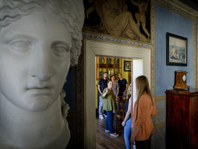 Huge bust of the goddess Juno in the foreground, guests moving through living spaces in the background