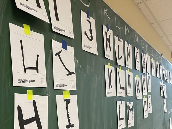 Eine Tafel, an der Zeichnungen von Buchstaben hängen.