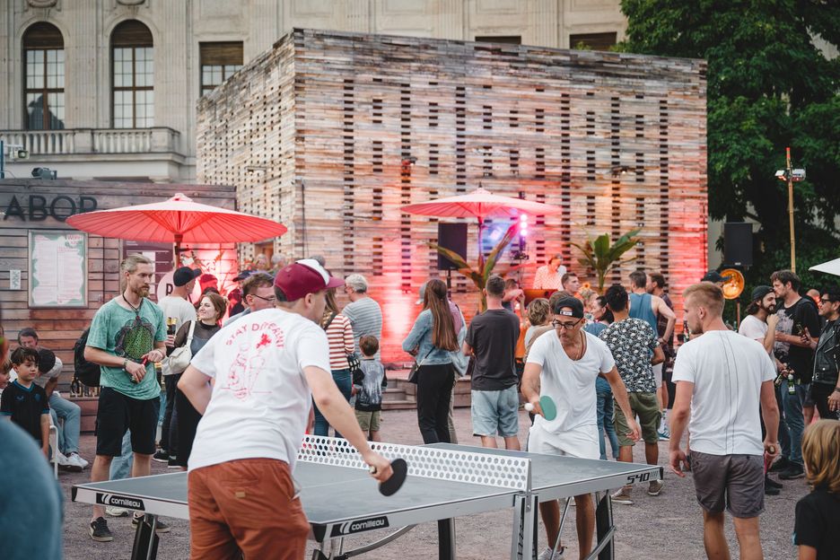 Table tennis at the Co-Labor Two people playing table tennis, guests at an event in front of the co-laboratory can be seen in the background