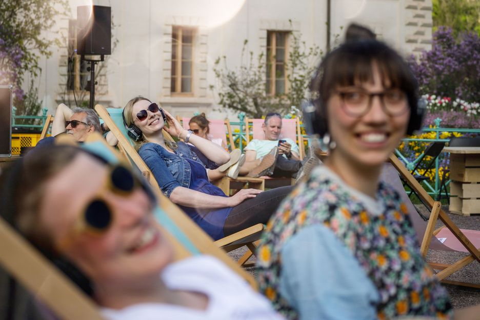 Zwei Frauen mit Kopfhörern, sitzend vor einem Holzkubus