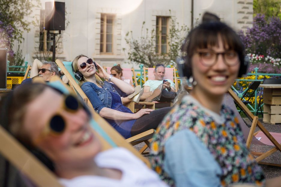 Zwei Frauen mit Kopfhörern, sitzend vor einem Holzkubus