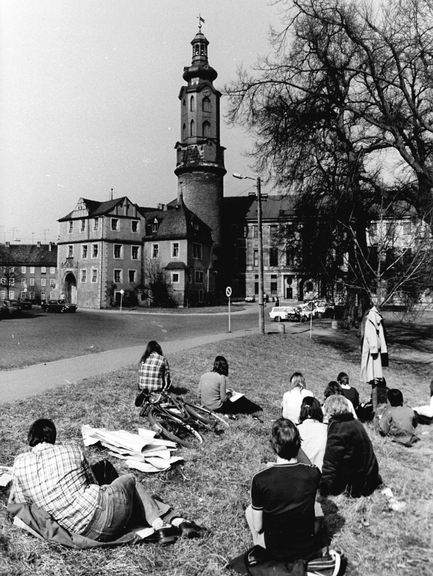 Schwarz-Weiß-Foto vom 01.04.1982: Auf der Wiese vor dem Schloss befinden sich Architekturstudierende, die das Schloss als Motiv für Zeichenübungen nutzen. Zitat:"Mit den ersten warmen Sonnenstrahlen kommen auch Weimarer Architekturstudierende ins Freie, um nach der Natur zu zeichen. Als willkommenes Objekt dient ihnen das Weimarer Schloss."