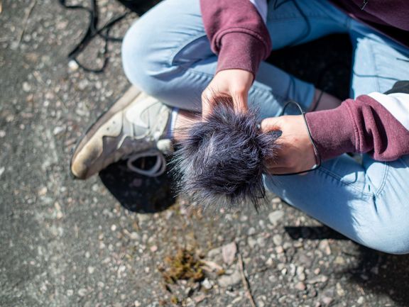 von oben fotografiert. Eine Person sitzt im Schneidersitz auf dem Boden und hält ein Mikrofon.