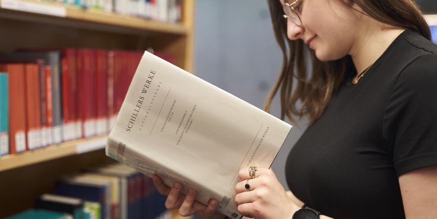 Eine junge Frau hält die Schiller-Nationalausgabe aufgeschlagen in der Hand und schaut hinein.